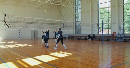 The volleyball players practice passing the ball over the net. Two female volleyball players come to the court with a ball and start warming up.