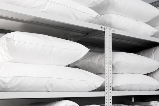 A white shelf with many white pillows stacked on top of each other. pillows are all the same size and color, and they are neatly arranged on the shelf. Concept of order and