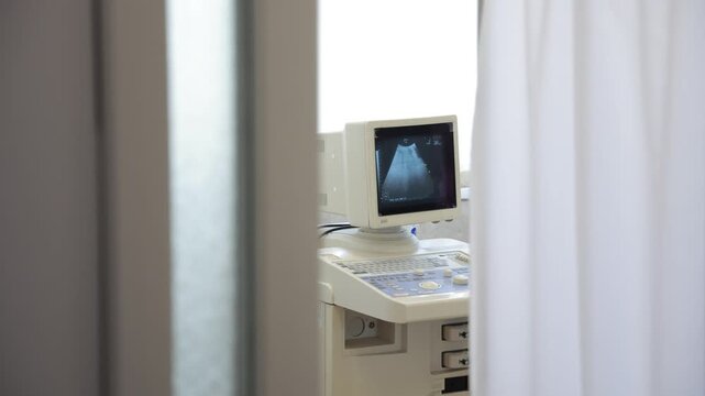 Footage showing an ultrasound machine screen partially obscured by curtains in a clinical setting.