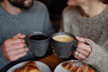Man and woman clinking coffee mugs during breakfast.