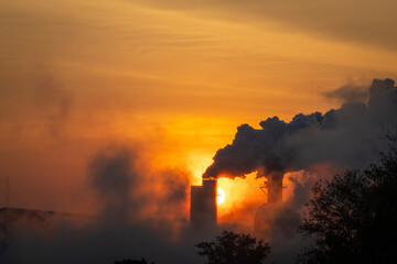 The silhouettes of industrial factories releasing smoke from their chimneys rise into the atmosphere, causing pollution in the early morning, environmental problems, air pollution.