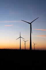 Four silhouettes of wind turbines producing wind energy at sunset