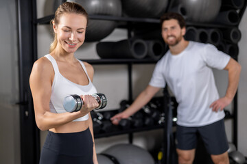 Fototapeta premium Woman in white top and black leggings exercising with the dumbbells in the gym