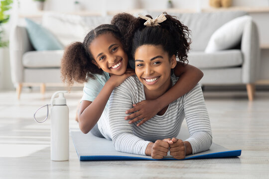 Portrait of athletic black mother and daughter bonding while exercising together at home during coronavirus pandemic, living room interior. Healthy family lifestyle, sport with kids concept - Powered by Adobe