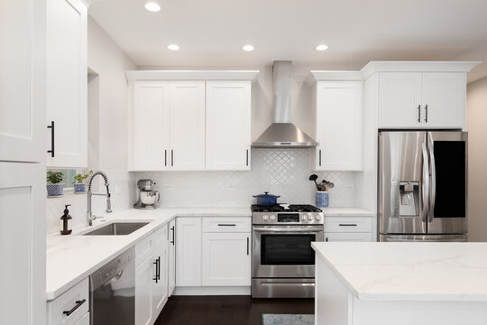 A beautiful kitchen detail with white cabinets, a gold faucet, white marble countertops, and a brown picket ceramic tile backsplash.
