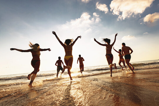 Group of happy young friends are having fun, runs and jumps at sunset sea beach. Tropical vacations concept