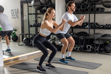 Fototapeta premium Two young people exercising in the gym in squatting position