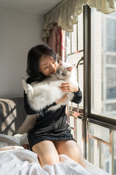  Woman Cuddling Fluffy White Ragdoll Cat by Window in Cozy Urban Apartment Bedroom Morning