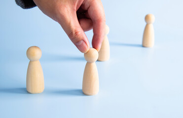 Hand selecting wooden figure depicting team member recruitment