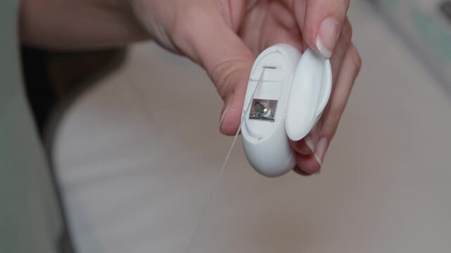 Woman&rsquo;s hands pulling and cutting a piece of dental floss from a white dispenser representing daily oral hygiene, dental care and health routine