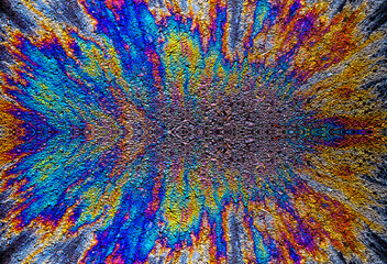 a photograph of an oil or petrol stain on a wet asphalt or pavement surface, a phenomenon called iridescence. interference of light waves reflecting off the different layers of the thin oil film