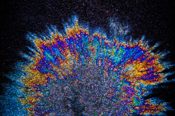 a photograph of an oil or petrol stain on a wet asphalt or pavement surface, a phenomenon called iridescence. interference of light waves reflecting off the different layers of the thin oil film