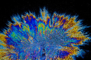 a photograph of an oil or petrol stain on a wet asphalt or pavement surface, a phenomenon called iridescence. interference of light waves reflecting off the different layers of the thin oil film