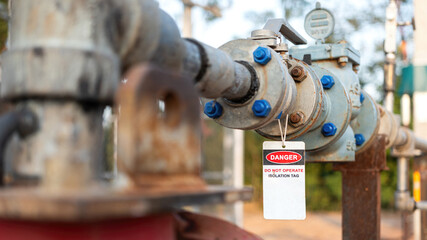 An isolation tag on oil production pipeline ball valve. This is lock out tag out safety sign to inform do not operate this equipment. Industrial safety sign object, close-up and selective focus.