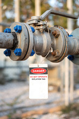 An isolation tag on oil production pipeline ball valve. This is lock out tag out safety sign to inform do not operate this equipment. Industrial safety sign object, close-up and selective focus.