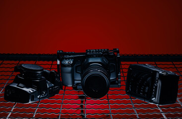 A camera and two other gadgets rest on a grid pattern with a dark red background. The arrangement highlights tools often used in photography and videography settings.