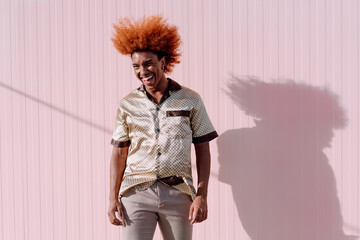 Laughing young African American man with curly ginger hair standing outdoors, hands in pockets, projecting joyful energy and modern urban confidence in a tech-driven lifestyle.