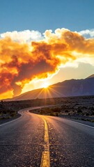 Winding road leads to a sunlit horizon behind mountains under a fiery, cloud-filled sky at sunset