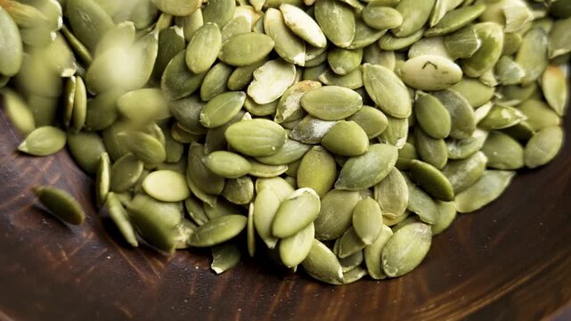 Dry green pumpkin seeds falling in slow motion into a wooden bowl. A nutritious organic product.
