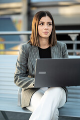Young businesswoman working on a laptop outdoors in the city, remote freelancer contemplating ideas for professional growth, modern connectivity and urban entrepreneurship