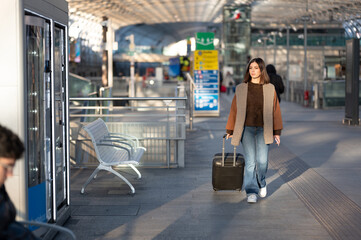 Young woman walking through a bright modern airport terminal with suitcase, moving toward departure or arrival in sleek glass-and-metal architecture, solo traveler on the go