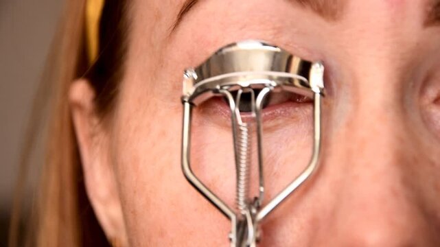 Woman curling eyelashes with silver metal curler tool close up