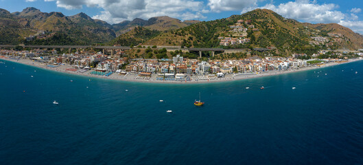 Fototapeta premium Aerial view of the small town of Letojanni, in the province of Messina, Sicily, Italy. It is a Sicilian coastal town and a beautiful tourist destination. In foreground is the blue Mediterranean Sea.