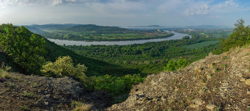 View of the winding river snaking through lush green landscapes, framed by rocky terrain and distant hills under a soft sky, Sturovo, Nitra Region, Slovakia.
