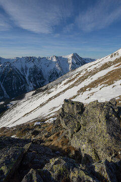 View of snow-dusted mountain peaks under a bright blue sky, observed from rugged, rocky foreground in the scenic landscape, Nizna Bystra, Slovakia.
