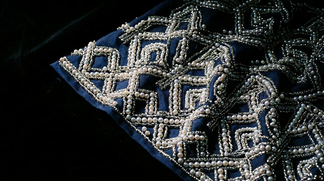 Intricate beadwork with pearls and silver thread on blue fabric, a detailed textile art piece.