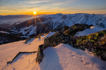 View of sunburst over the snow-capped peaks, illuminating the jagged rocks and valleys in a serene winter landscape, Nizna Bystra, Zilina Region, Slovakia.