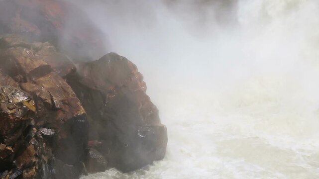 Powerful water flows from Maneri Dam on the Bhagirathi River, creating mist and strong currents across rocky terrain in the Himalayan region near Uttarkashi, Uttarakhand.