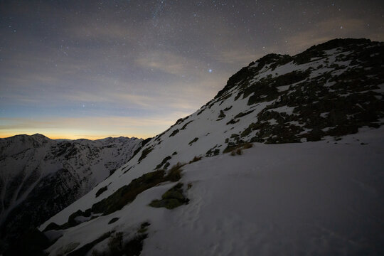 View of a snow-covered mountain slope under a starlit sky with a touch of dawn's glow on the horizon, Nizna Bystra, Slovakia.