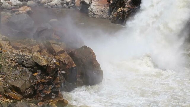 Powerful water flows from Maneri Dam on the Bhagirathi River, creating mist and strong currents across rocky terrain in the Himalayan region near Uttarkashi, Uttarakhand.