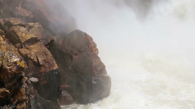 Powerful water flows from Maneri Dam on the Bhagirathi River, creating mist and strong currents across rocky terrain in the Himalayan region near Uttarkashi, Uttarakhand.
