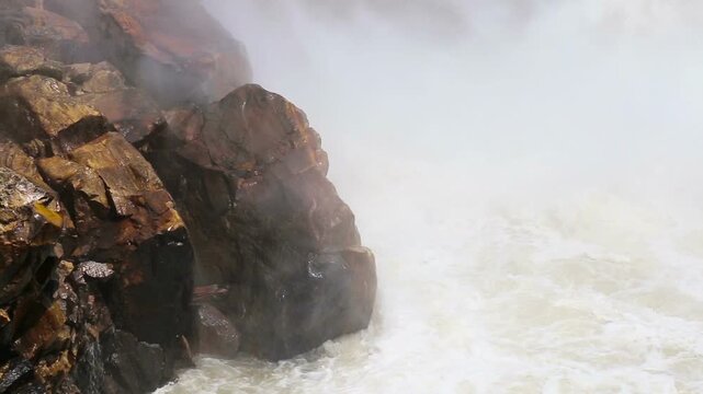 Powerful water flows from Maneri Dam on the Bhagirathi River, creating mist and strong currents across rocky terrain in the Himalayan region near Uttarkashi, Uttarakhand.