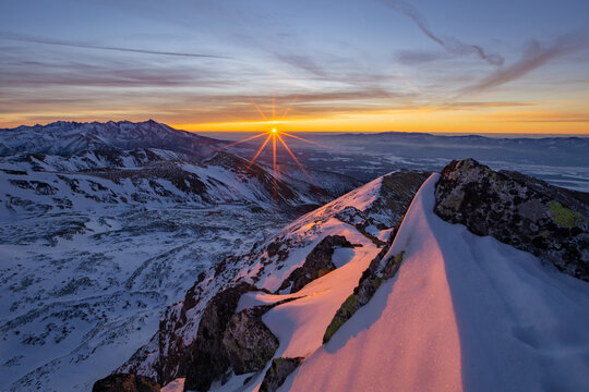 View of the sun bursts over the snow-laden peaks of the Western Tatras, casting an orange and pink glow on the landscape, Nizna Bystra, Zilina region, Slovakia.
