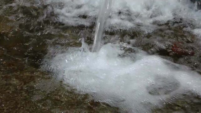 Clear mountain spring water pours forcefully into a shallow stream, showing natural freshness, purity, and continuous water flow from a Himalayan source in Uttarakhand, India.