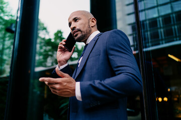 Side view of African-American businessman on smartphone call, gesturing while speaking, emphasizing...