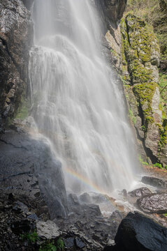 View of cascading waterfall with a faint rainbow at its base, framed by mossy rocks and lush greenery, creating a serene scene, Polana, Banska Bystrica Region, Slovakia.