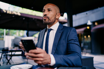 Serious businessman holding smartphone and coffee, gazing forward with clarity, conveying balance...