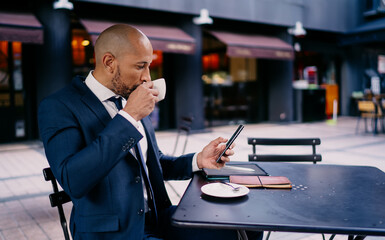 Businessman sipping coffee while checking smartphone, showing concentration, digital consumption and seamless integration of mobile habits in modern professional rhythm.