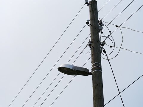 A wooden utility pole with a street light and a tangle of power and communication lines set against a overcast sky.