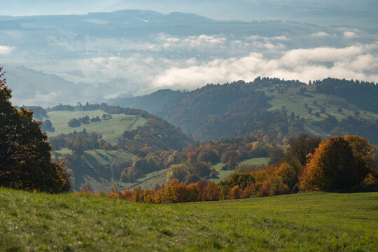View of rolling hills cloaked in morning mist, vibrant autumn trees dotting the landscape under a soft sky, a tranquil scene, Selce, Banska Bystrica Region, Slovakia.