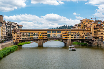 View of Ponte Vecchio in Florence (Ponte Vecchio, Firenze) and nearby buildings along the Arno River on a bright summer day, capturing the historic charm and vibrant riverside scene.