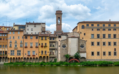 View of Ponte Vecchio in Florence (Ponte Vecchio, Firenze) and nearby buildings along the Arno River on a bright summer day, capturing the historic charm and vibrant riverside scene.