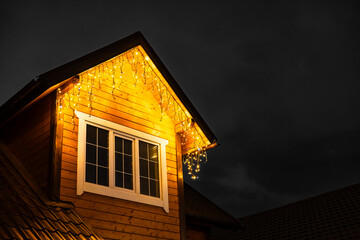  a fragment of a house decorated with electric garlands. decorating the house facade with garlands. New Year's home decoration. the roof of the house decorated with a garland. 