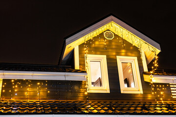  a fragment of a house decorated with electric garlands. decorating the house facade with garlands. New Year's home decoration. the roof of the house decorated with a garland.  