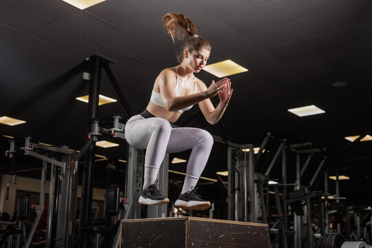 Athletic woman performing plyometric box jump workout in indoor fitness gym