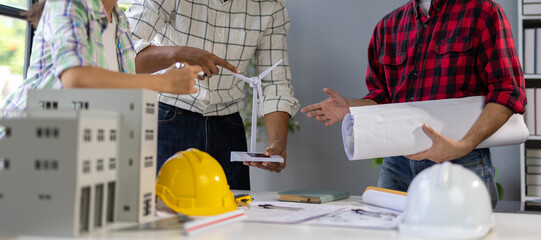 Engineers discussing about wind turbine and building model during meeting.